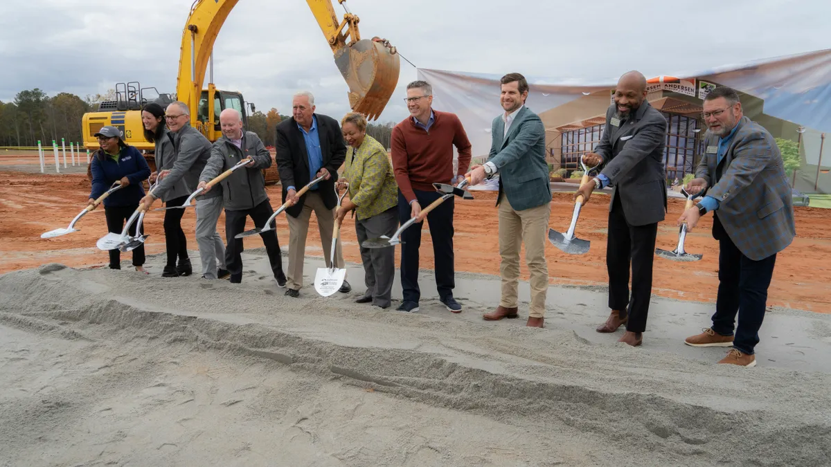 Several people in business attire pose with shovels in hand for a groundbreaking photo.