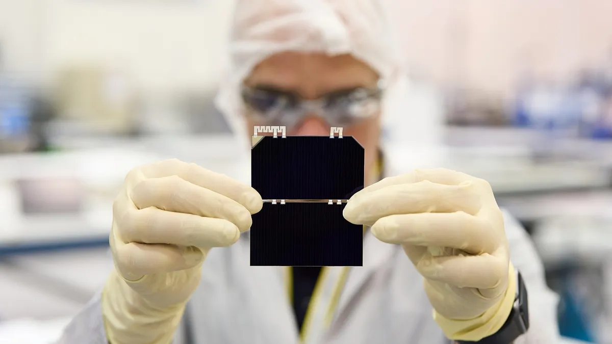 A person in personal protective equipment holding a solar chip.