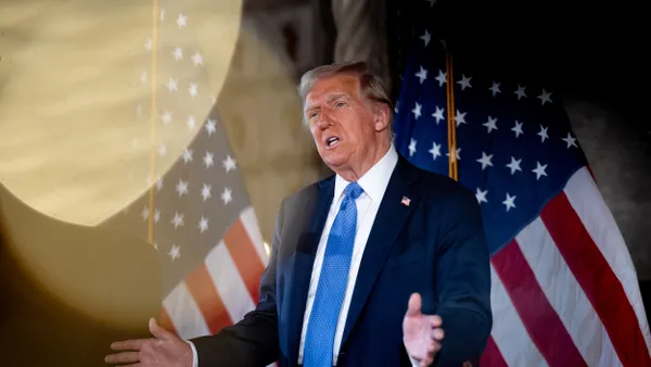 President-elect Trump stands between two American flags, speaking with his hands gesturing widely.