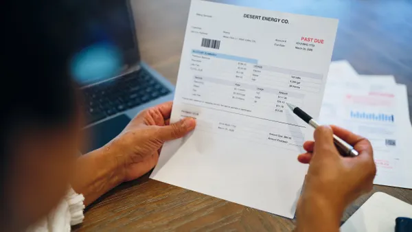 A person's hands holding a paper bill that says "Desert Energy Company" with a red "Past Due" stamp.