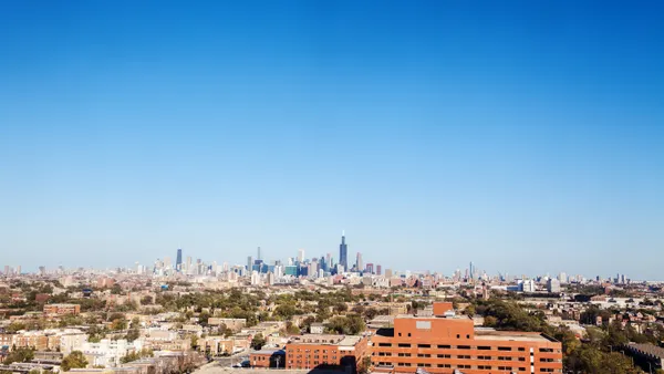 A sparse suburban neighborhood with skyscrapers in the distance under a blue sky.