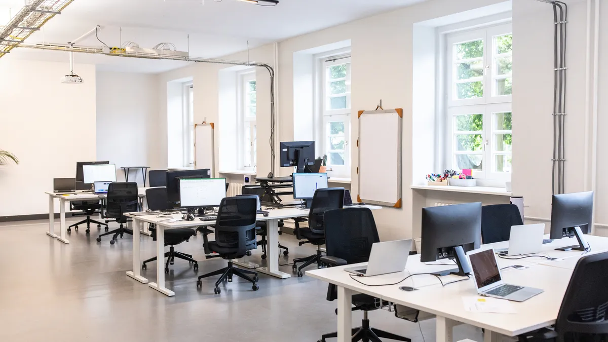 Interior of a coworking office space with computers and laptops in desks. Modern open plan office with no people.