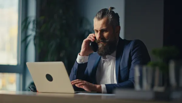 A person in a business suit on their laptop and talking on the phone