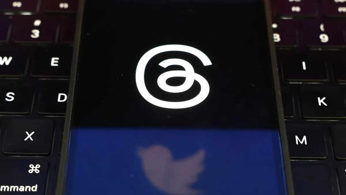 A reflection of the Twitter logo cast on a phone screen emblazoned with the Threads logo