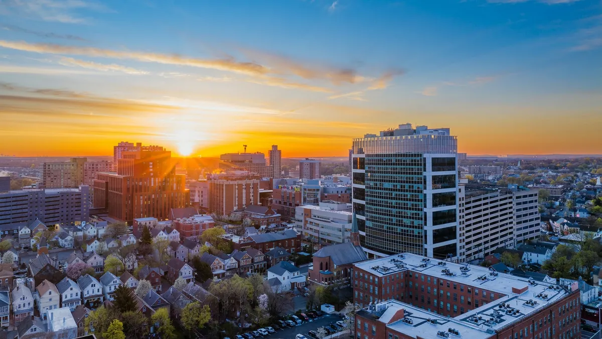 Sunset over an urban skyline with high-rise buildings and residential houses, casting a warm glow and creating a serene, picturesque atmosphere.
