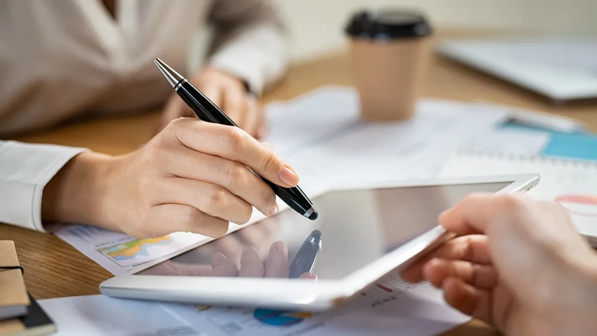 Digital signature on tablet. Close up of hand of young businesswoman signing documents on digital tablet with pen. Business woman hand pointing digital tablet with pen while working at desk.