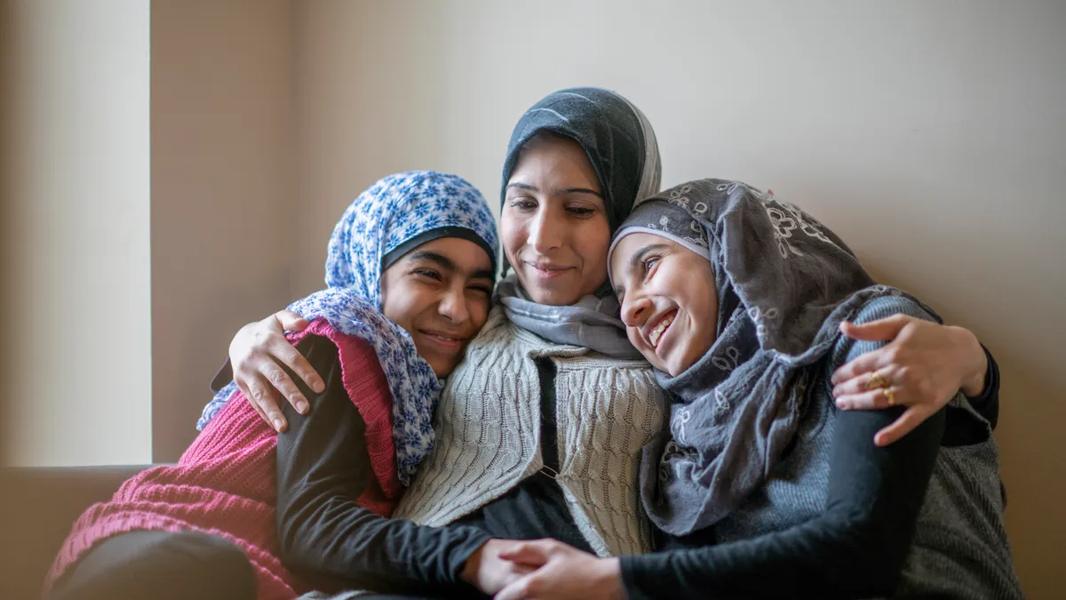 A hijabi mother embraces her two hijabi kids