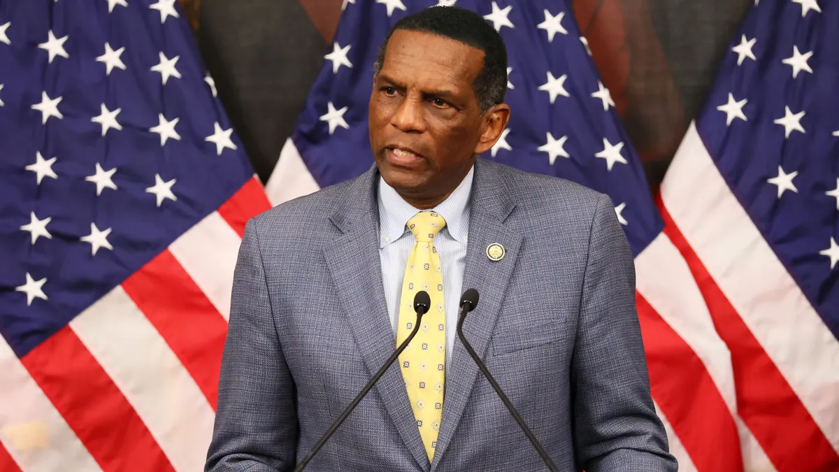 Burgess Owens speaks at a podium with American flags in the background.