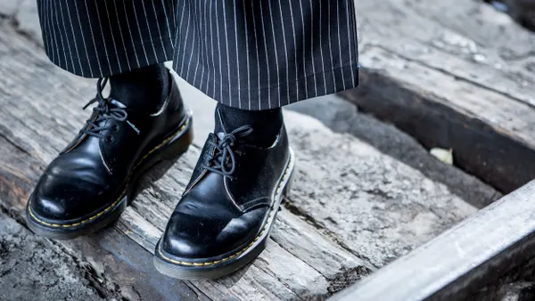 A closeup of a person's Dr. Martens oxfords. They are wearing black socks and wide legged striped pants.