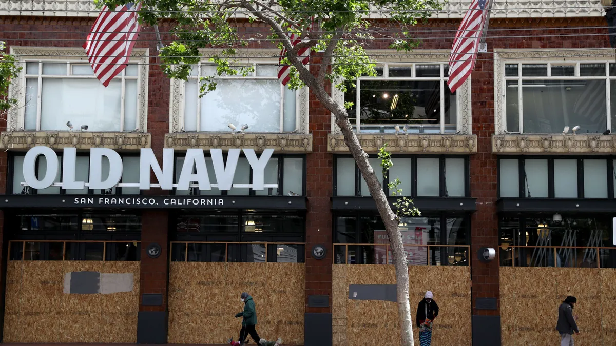 Shoppers walk by boarded-up windows in front of a brick, Old Navy building.