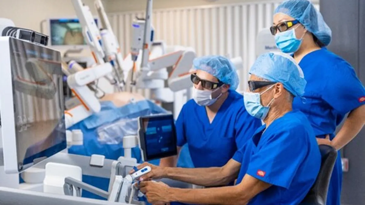 Three clinicians in surgical garb view the screen at the console of Medtronic's Hugo robotic surgery system.