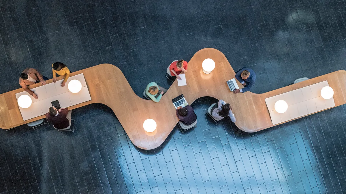 Panoramic overhead view of several business meetings going on in the communal area of a modern office building.