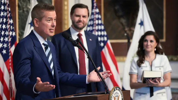 Two men in suits and a woman in the background.