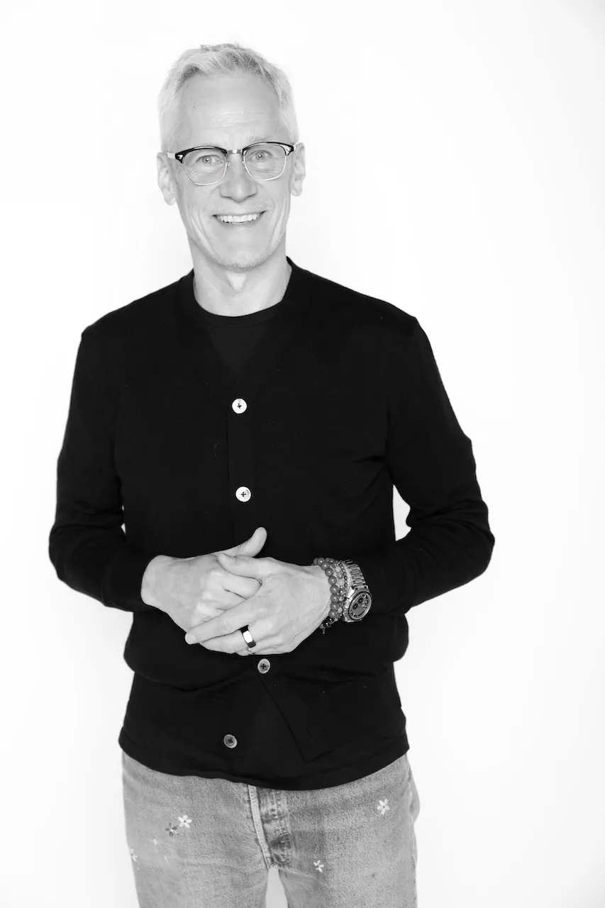 Matt Bolte, wearing a cardigan and light jeans, smiles at the camera in a black-and-white photo.