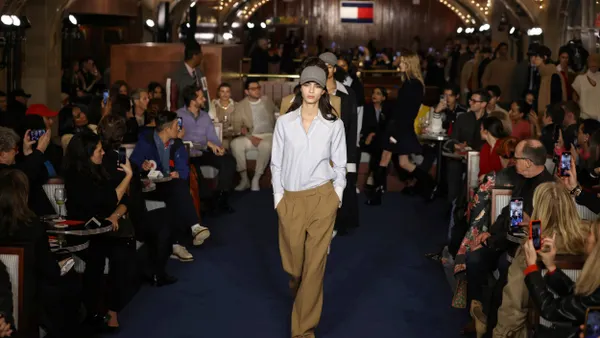 A model wears a baseball hat, button down shirt and pants on a runway.