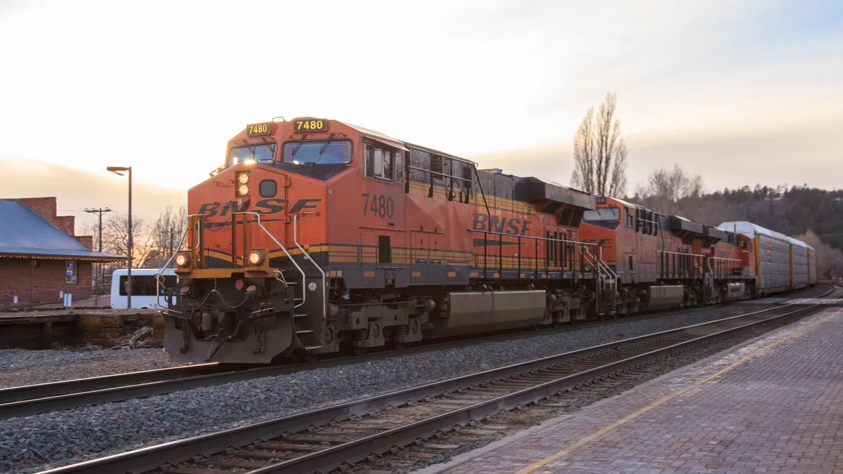 An orange BNSF freight locomotive pulls a train through a station.