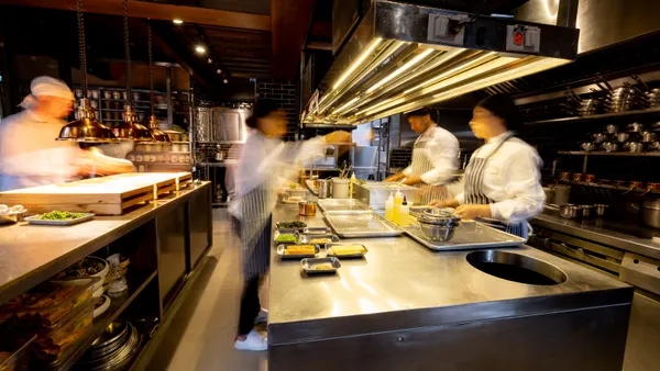 An image of back-of-house workers preparing meals in a kitchen. Their faces are blurred