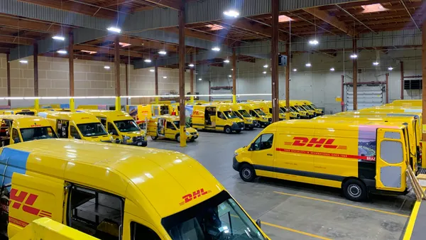 A fleet of DHL-branded yellow trucks are parked in a warehouse.