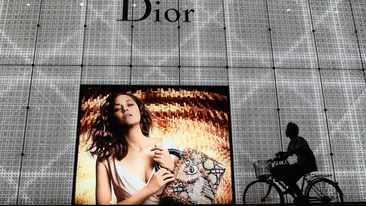 In the evening a man rides bicycle past a large advertisement for a Christian Dior store in Beijing, China.