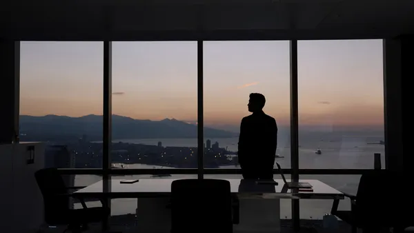 A man stands in a board room, looking out on the horizon