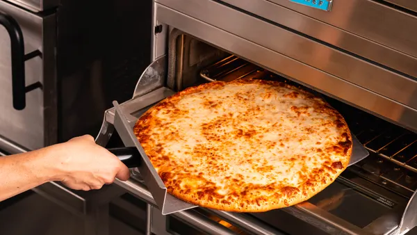 A photo of a cheese pizza from McLane Company's Prendisimo line being put into a pizza oven.