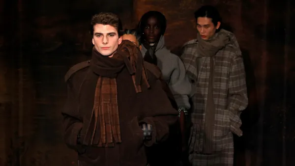 Models in plaid outerwear and scarves walk down a runway.