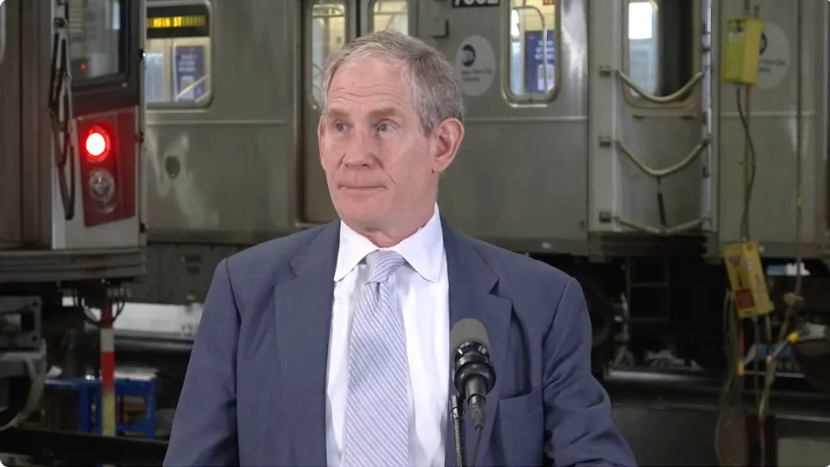 A man at a podium in front of a subway car.