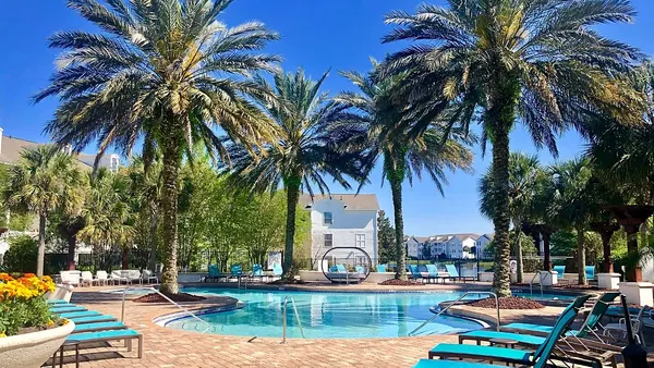 Pool and palm trees and white apartments in the background.