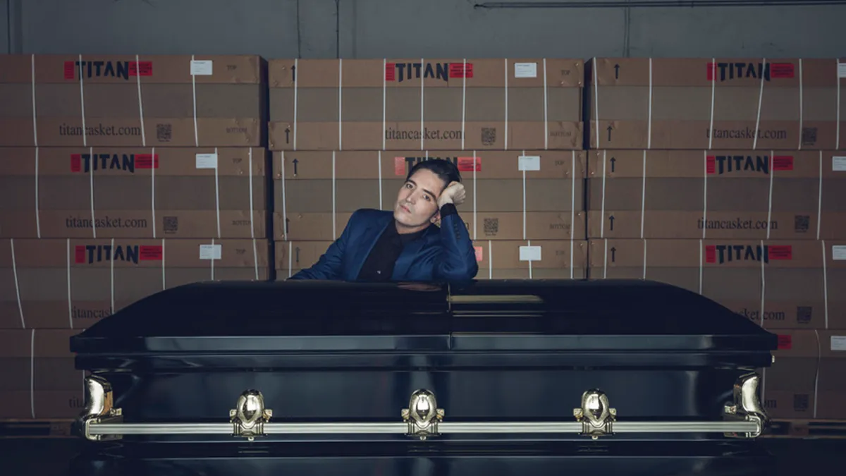 Actor David Dastmalchian wearing a black suit posing on a black and metal casket