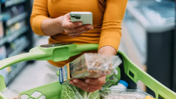 Woman scans food label in front of a shopping cart