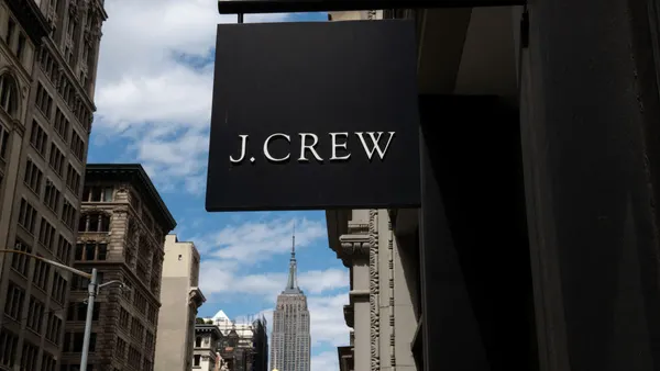 A black sign with the words "J. Crew" hangs from a building on a city street.
