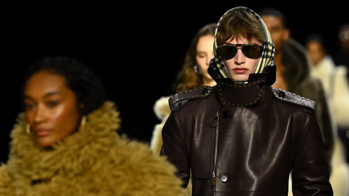 A model in sunglasses and a head scarf walks the runway.