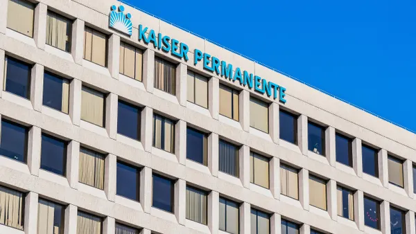 A beige office building with large rectangular windows and vertical blinds, featuring a “Kaiser Permanente” sign near the rooftop.