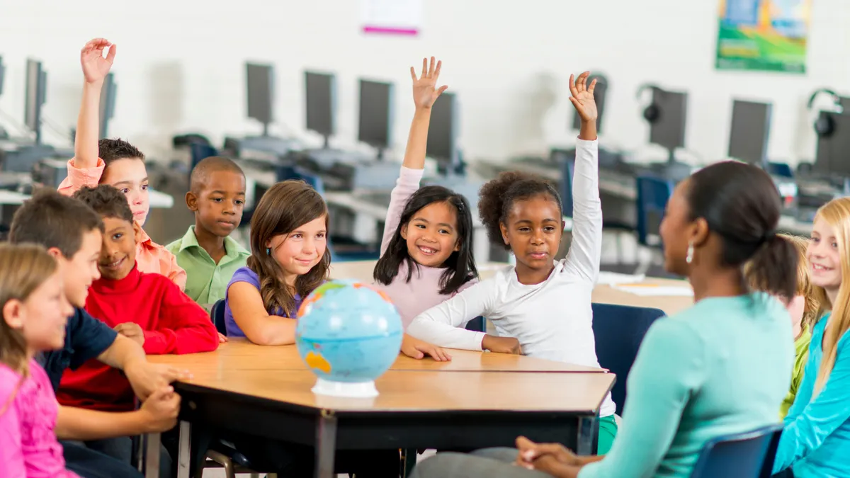 A multi-ethnic group of elementary age students are learning the places of the world by looking at a globe in geography and history class.