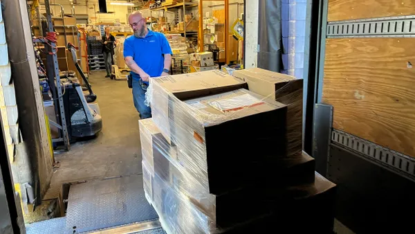 A person pulls a shipment out of the back of a trailer onto a loading dock.