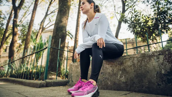A woman in Puma running shoes sits on a bench.