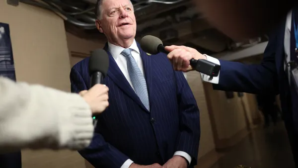 A person wearing a blue suit talking as two people hold microphones in front of him.