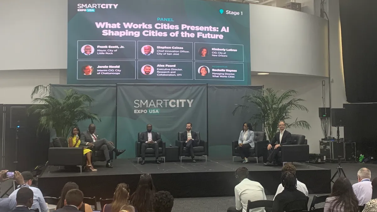 Six people sit on chairs on a stage in front of an audience. A presentation behind the speakers reads "What Works Cities Presents: AI Shaping Cities of the Future"