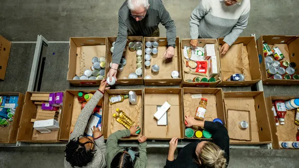 A small group of Volunteers are seen working together at a local food bank as they pack donations. They are each dressed casually and working diligently together in this aerial view.