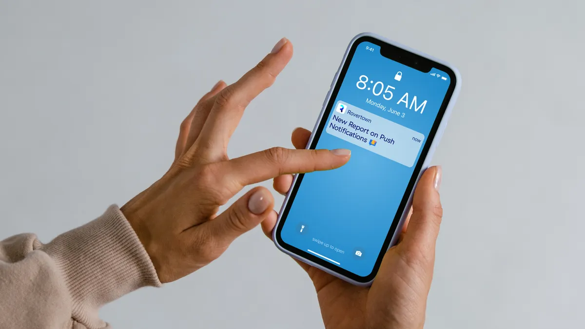 A photo of a hand holding a mobile phone. A notification on the phone reads "Rovertown: New Report on Push Notifications"