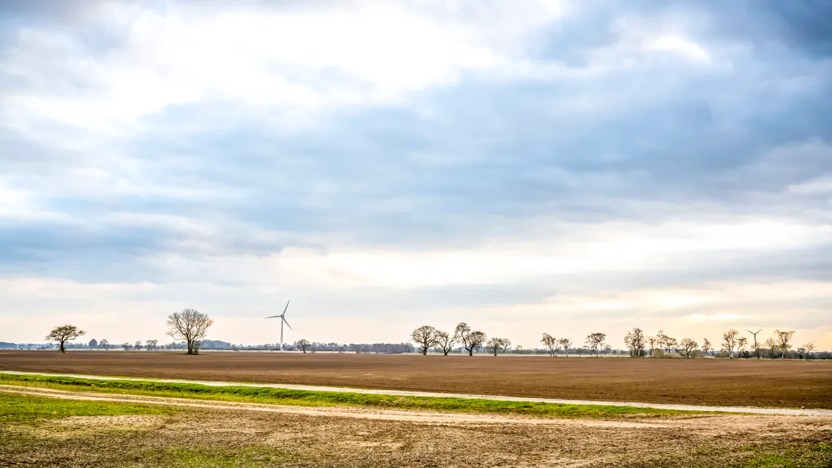 Blue sky above a farm field with wind turbine and trees in the distance