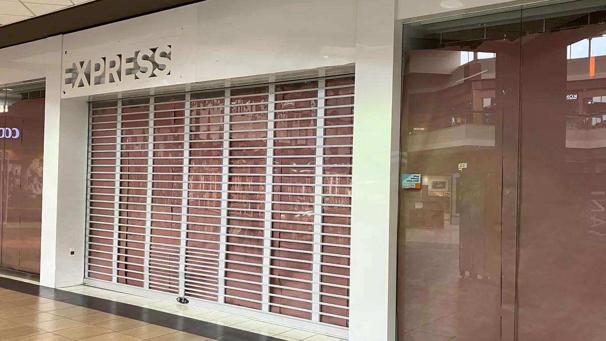 A former Express apparel storefront in a mall is closed, with the gate down and windows covered.