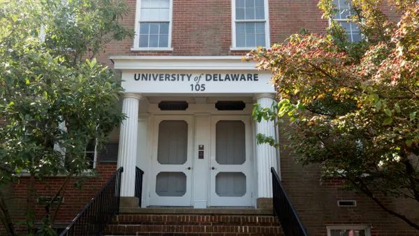 A red brick building with white doors and a tree on each side.