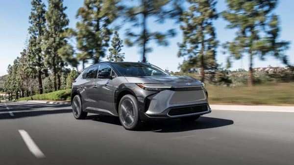 A 2025 Toyota bZ4X electric SUV driving on a road with tall trees in the background.