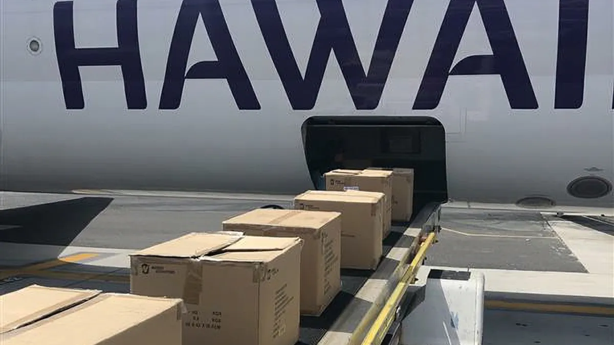 Boxes of relief supplies are being loaded into the belly of a Hawaiian Airlines aircraft.