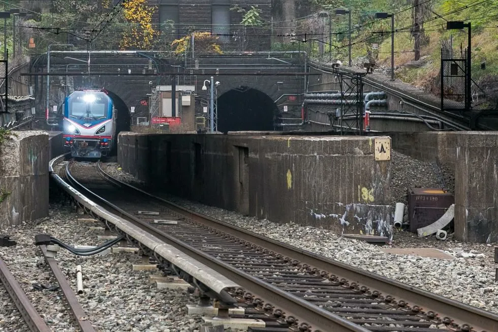 A blue and silver train emerges from a stone tunnel.