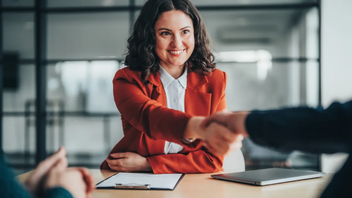 A woman in a blazer shakes hands in the office