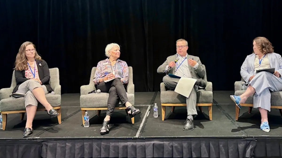 Four people are sitting in chairs on a stage. One person has a microphone.