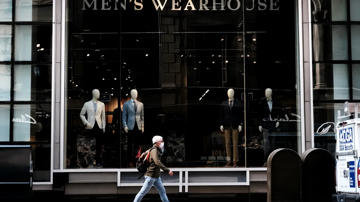 A person walks by a storefront window. The words "Men's Wearhouse" are displayed on the store window.