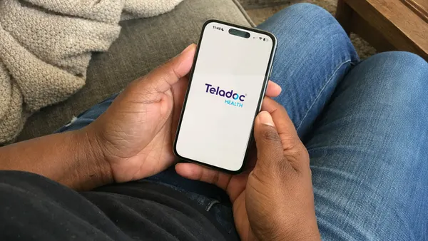 A person holding a smartphone with the Teladoc Health logo.